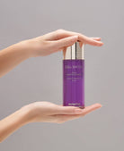 Essence revitalisante visage Cell Shock Swissline tenue entre deux mains, flacon violet, soin dynamisant et éclat.